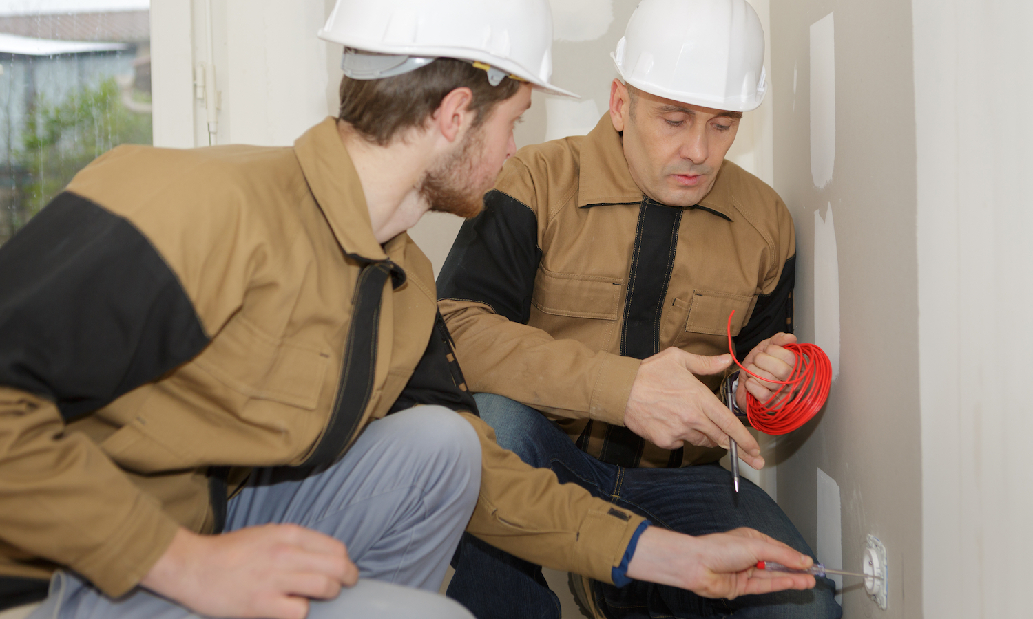hiring electrician - apprentice with supervisor holding cable by plug socket
